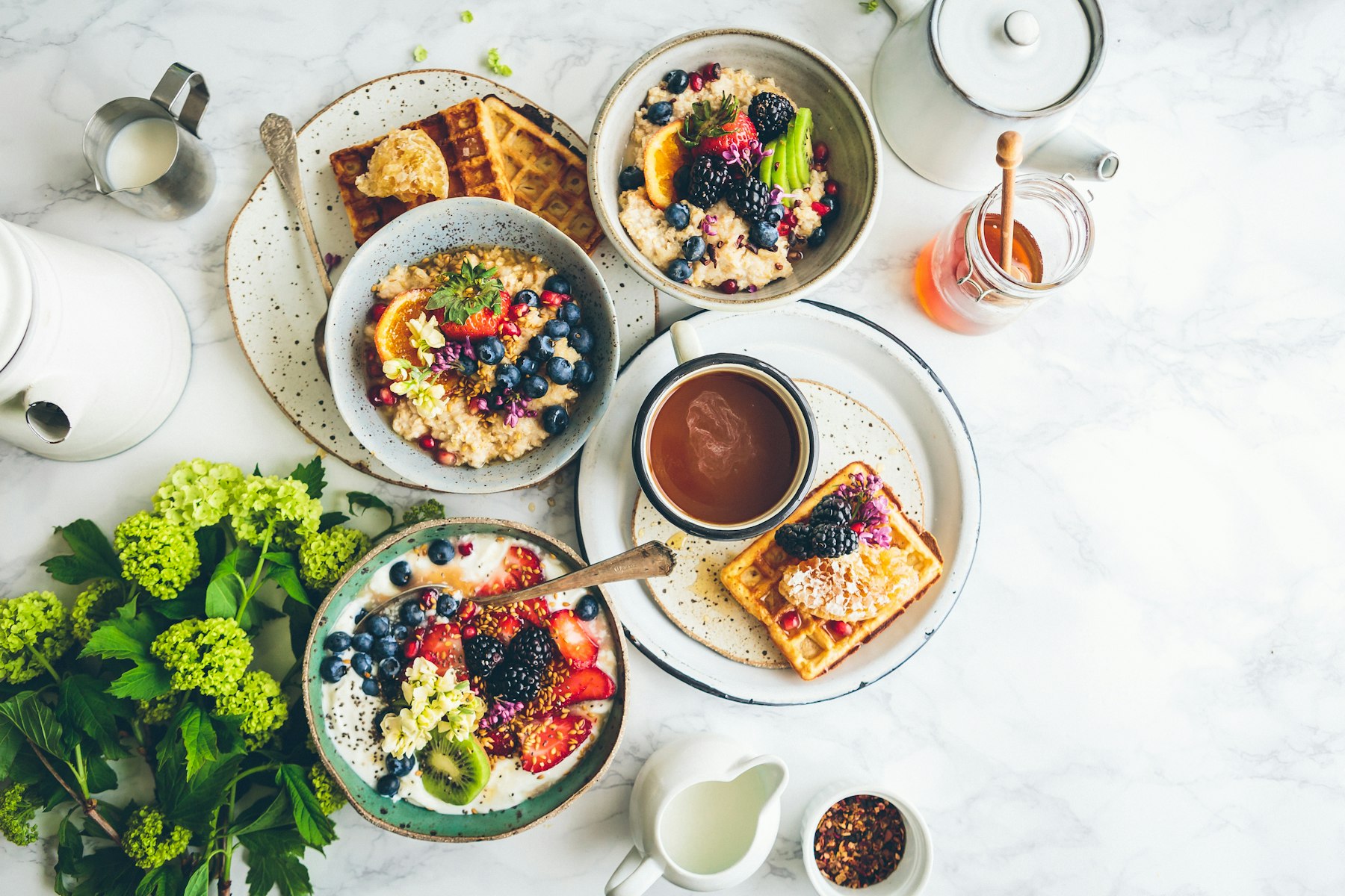 Breakfast table: yogurt and granola bowls, waffle with berries, honey, orange juice, coffee